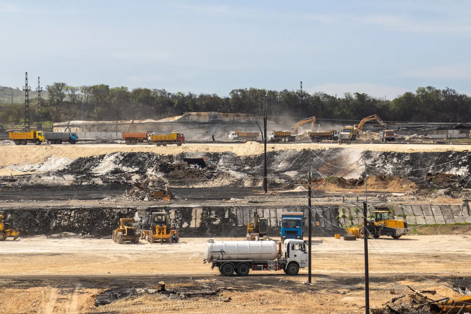 A group of construction trucks working at the site, with a mobile refueling truck delivering fuel to the machines