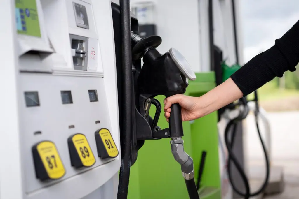 A woman reaches for a gasoline pump nozzle at a fuel station