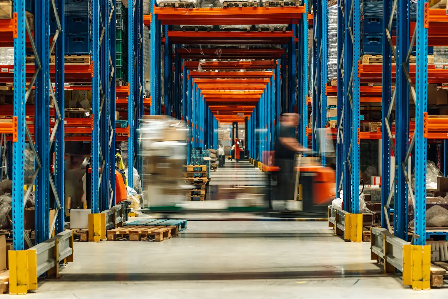 Warehouse workers are operating forklifts, transporting goods between tall shelves filled with various products, showcasing the fast paced environment of a modern distribution center